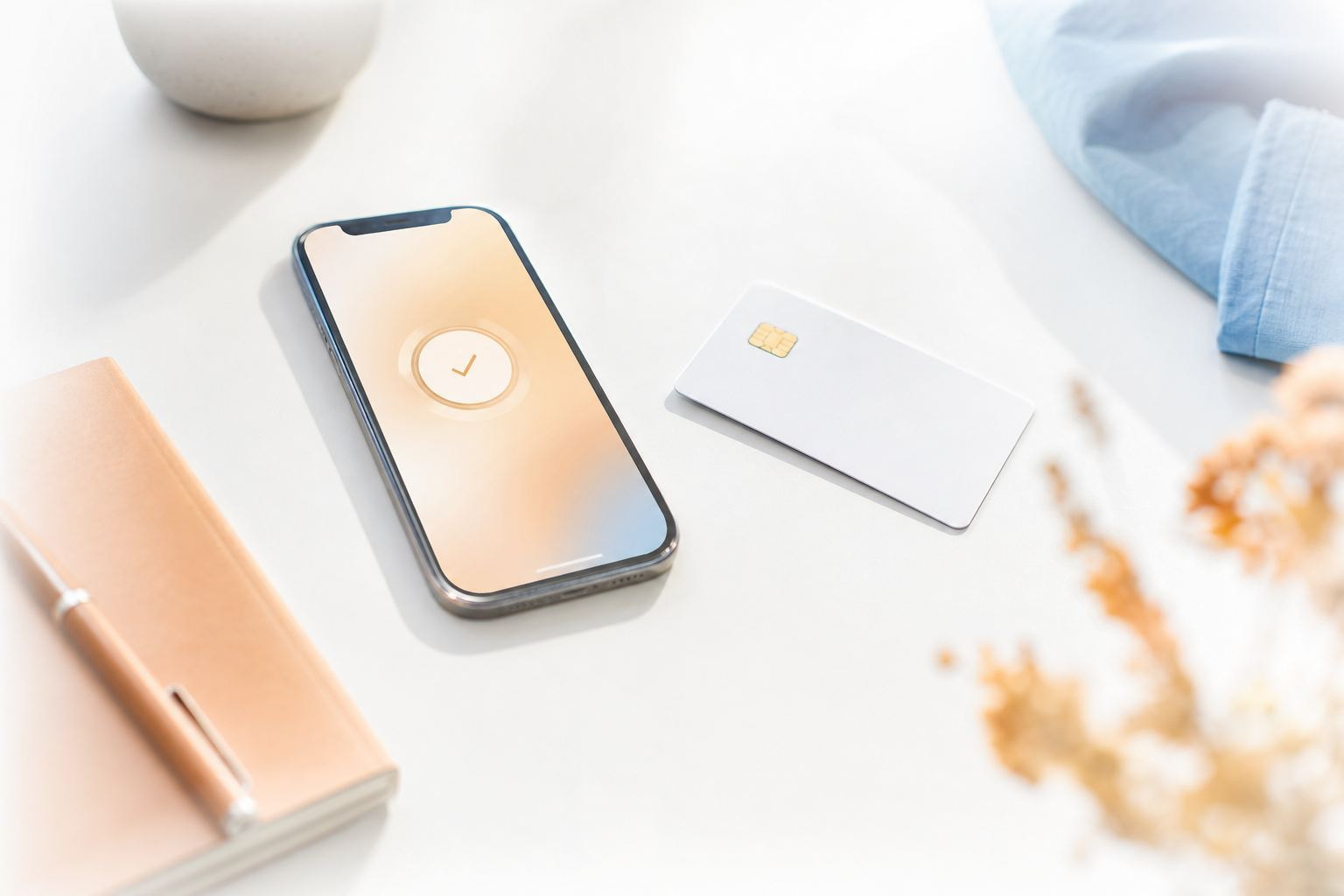 Helle Aufnahme eines Smartphones mit Bezahl-App neben einer schlichten Bankkarte auf weißem Schreibtisch
